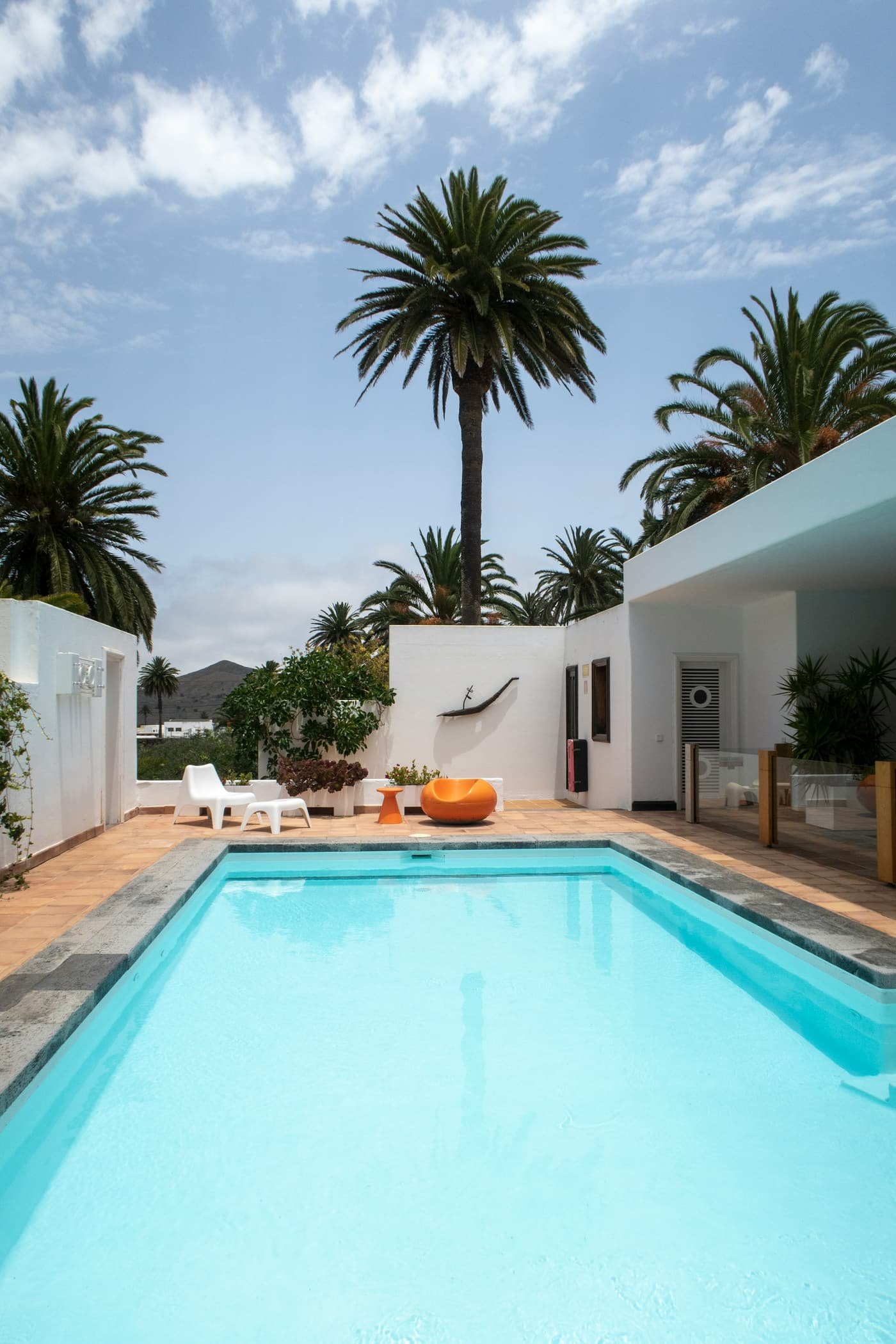 Long turquoise pool beside a white stucco house and tall palm